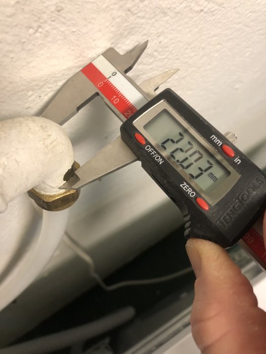 Mätning av anslutningsdimension R25 på en tvättmaskin med digital skjutmått.