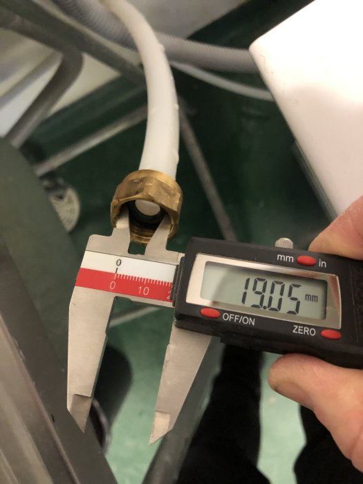 Skjutmått mäter diameter på en vit röranslutning med en mässingskoppling framför en tvättmaskinslang.