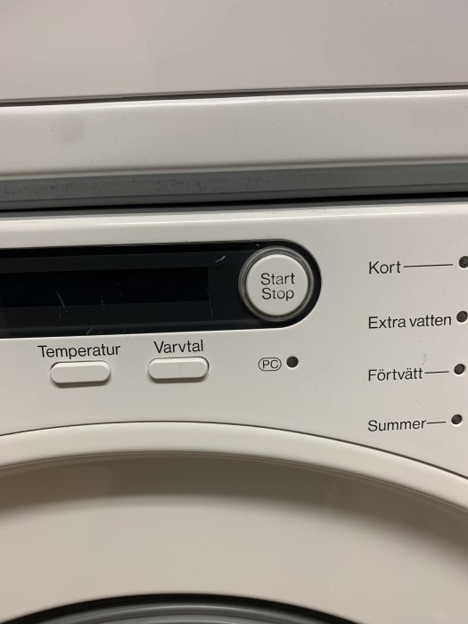 Närbild på en Miele tvättmaskins kontrollpanel med start/stop-knapp och olika programval.