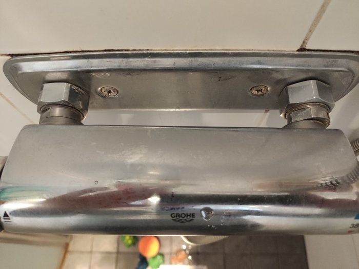 Närbild på muttrar och anslutningar för en fast monterad duschstång på ett badrumsvägg.
