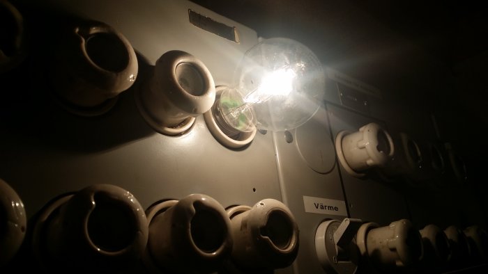 Tänd glödlampa i porslinssockel bland oanvända porslinssocklar på en elcentral.