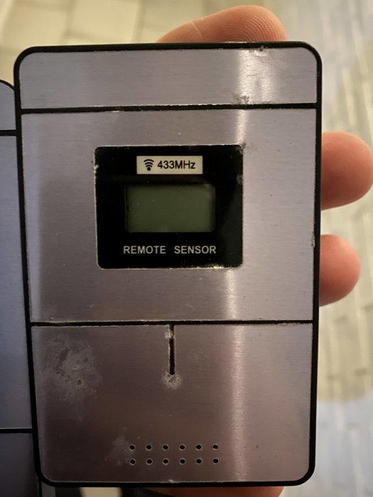 Hand håller en trådlös termometer märkt "433MHz" och "REMOTE SENSOR" som störtade andra enheter.