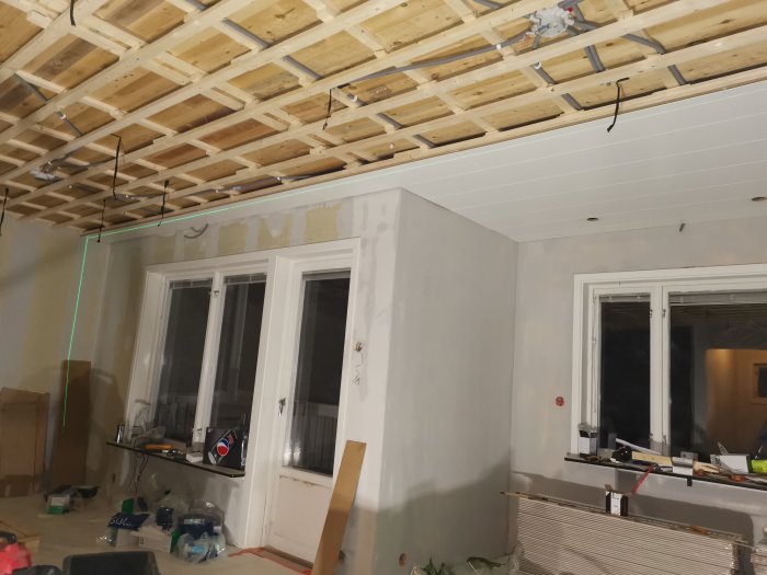 Inre rum under renovering med synliga träbjälkar i taket och en grön laserlinje som markerar en rät linje.