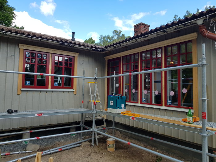 Renoverat hus med nydesignade, rödmålade fönsterfoder mot en grå fasad med ställning framför.