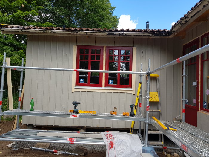 Hus under renovering med röda fönster som ska målas, byggställning och verktyg framför.