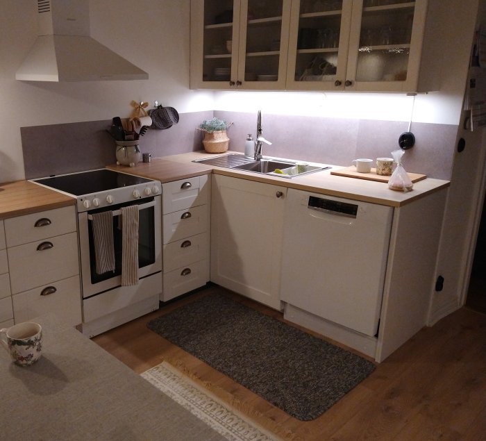 Kök med vita skåp och Ikea Omlopp bänkbelysning under överskåp, träbänkskiva och inbyggda vitvaror.