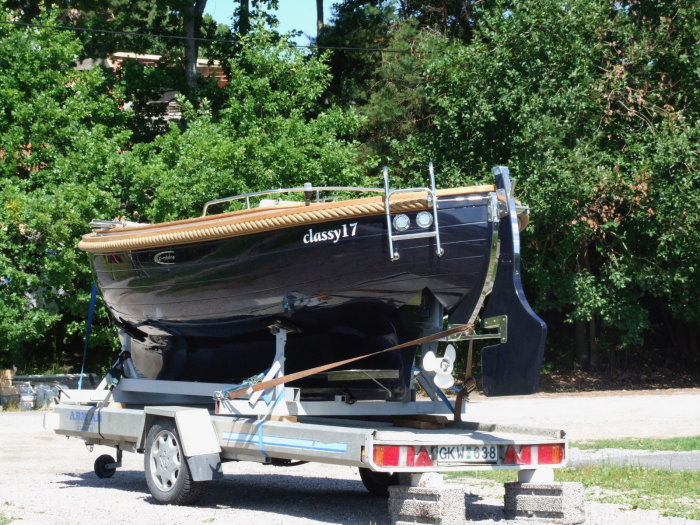 En svart 17-fots snipa "Grodan" med teakdäck på en släpvagn, utrustad med en Honda utombordsmotor.