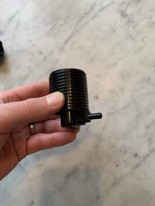 Hand håller en svart lampsockel med knapp på sidan mot en marmorbakgrund.