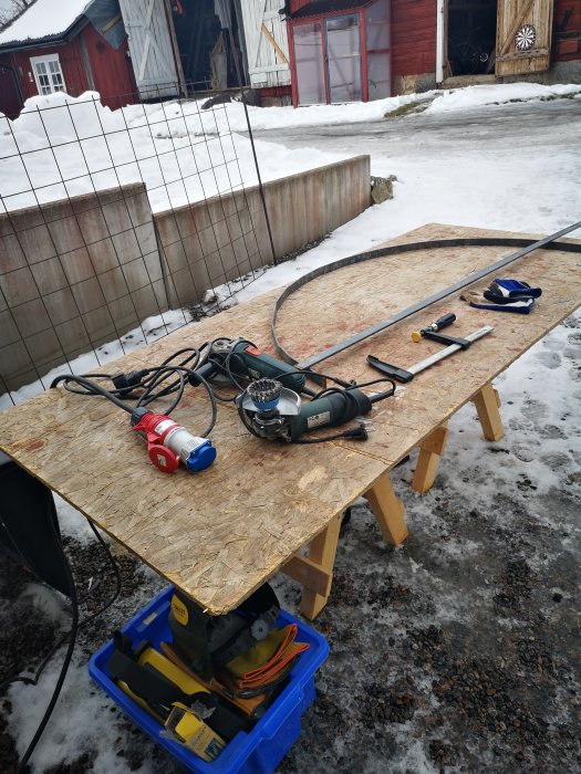 Svetsutrustning och verktyg på ett bord utomhus med snötäckt gård i bakgrunden.