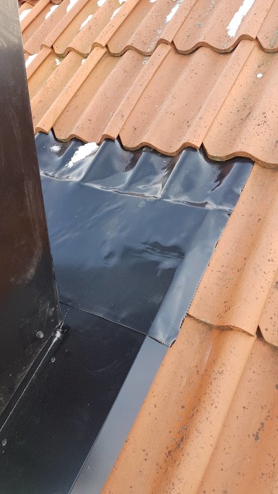 Närbild på takpannor med en taklucka eller tätning och del av skorsten.