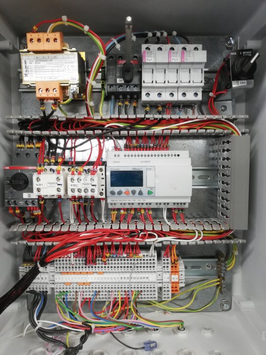 Välorganiserat styrskåp med transformator, säkringar, kontaktorer, motorskydd, brytare och PLC-plintar.