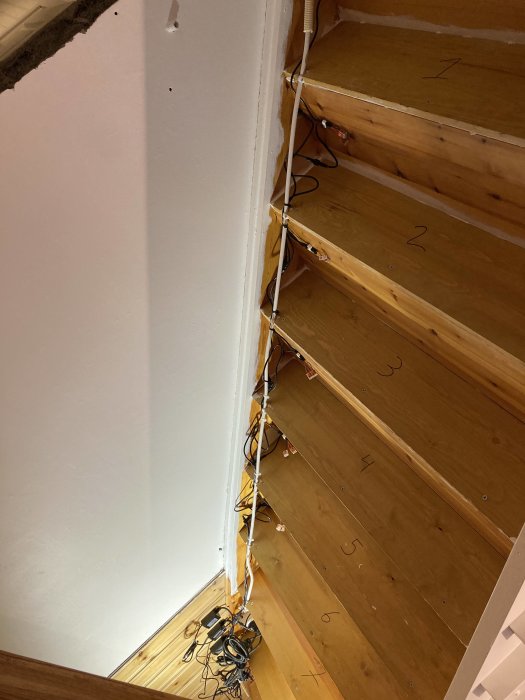 Osedda kabeldragningar och elektriska installationer längs en trätrappa under renovering.