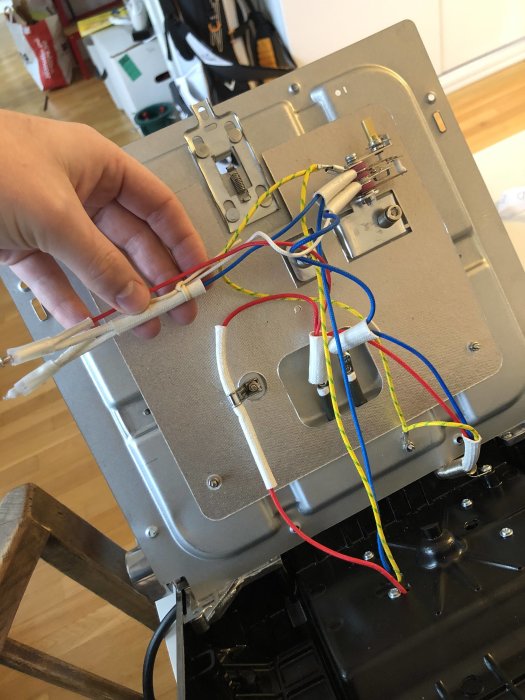 Elektriska kablar kopplade till baksidan av en apparat med en hand som håller i dem.