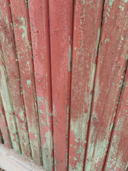 Närbild av en faluröd fasad med flagande färg som visar underliggande gröna lager.