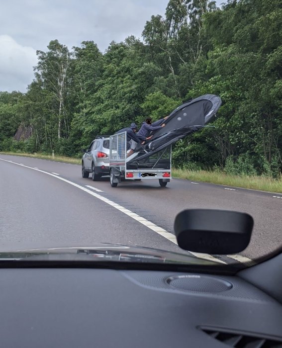 Studsmatta lyfts av vinden och fastnar på en släpvagn bakom en bil på en väg omgiven av grönska.