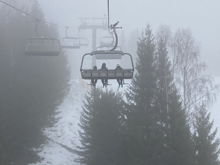 Skidlift med åkare i dimmigt vinterlandskap och snötäckta träd.