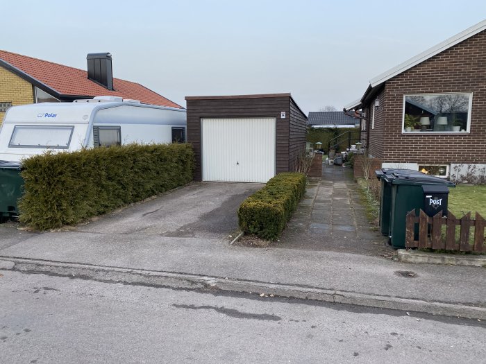Gammal uppfart med asfalt, plattor och höjdskillnad vid hus och garage.
