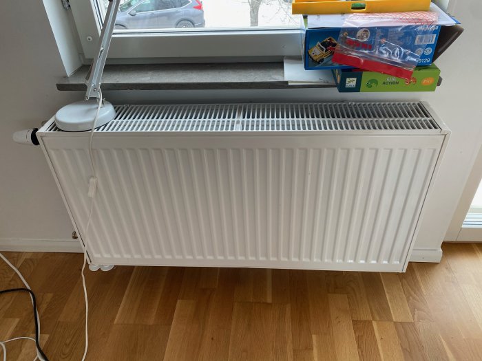 Vit radiator under ett fönster i ett rum med leksaker på fönsterbrädan.