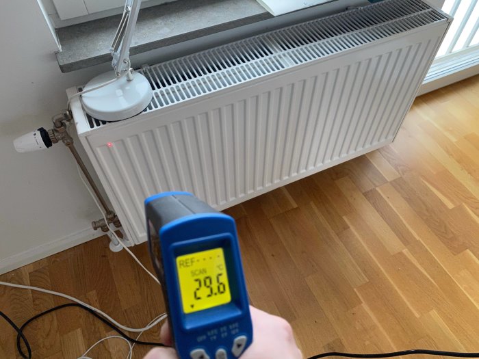 Värmekamera mäter temperaturen på ett kallt element i ett rum, visar 23,6°C, med parkettgolv och vit vägg i bakgrunden.