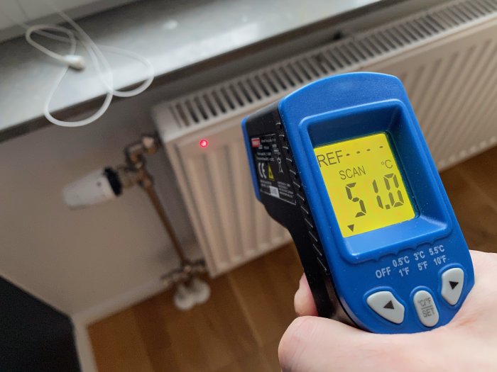 Handhållen värmekamera visar en temperatur på 5.1 grader Celsius framför ett element i ett rum.
