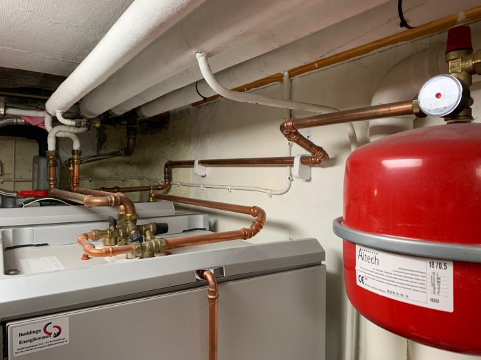 Värmepumpens kopparledningar och tryckmätare i ett pannrum, trycket visas under normal.