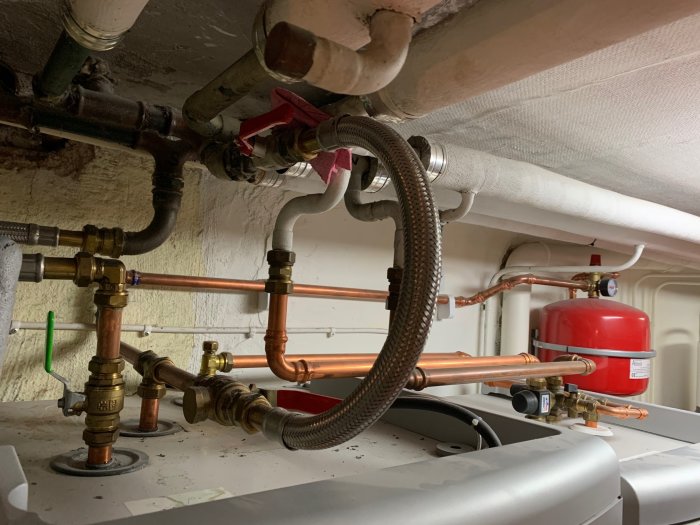 Värmeinstallation med kopparledningar, ventiler och röd expansionskärl.