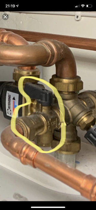 Påfyllningsventil markerad med gult på ett nätverk av kopparledningar och ventilkomponenter.