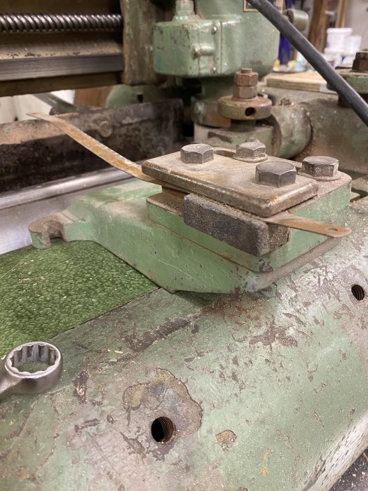 Metalldel med bultar på en grön maskin, användare frågar om delens funktion eller användningsområde.