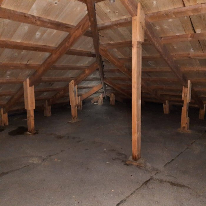 Insida av välanvänt vindutrymme med trästomme, stolpar, snedsträvor och mörka fläckar vid stolpfötter.