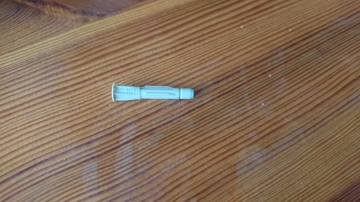 Plugg med vingar storlek 6x38 som ligger på ett trägolv.