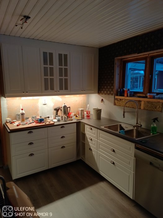 Kök under renovering med vita skåp och lådor, diskho, bänkskiva och verktyg utspridda.