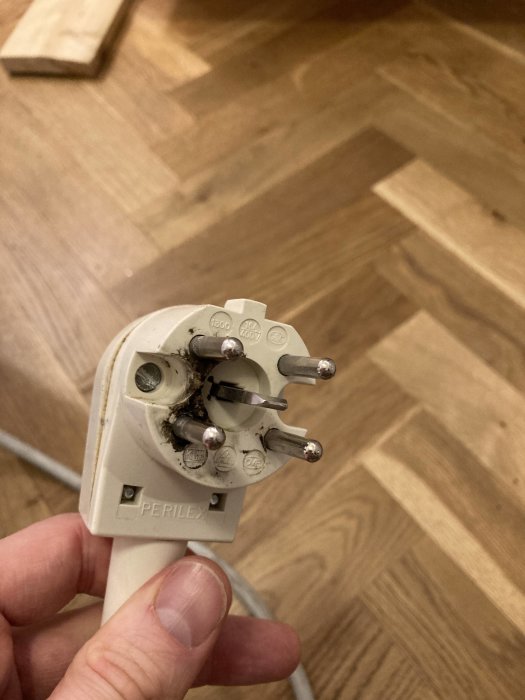 Hand som håller en Perilex stickpropp med brännskadade kontakter och smältskador.