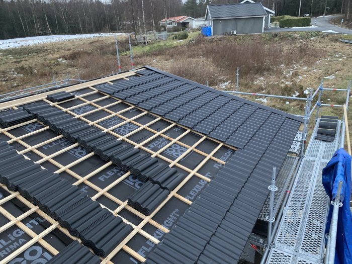 Tegeltak under installation med svarta Jönåker Protector-tegel och synlig byggställning på en byggplats.