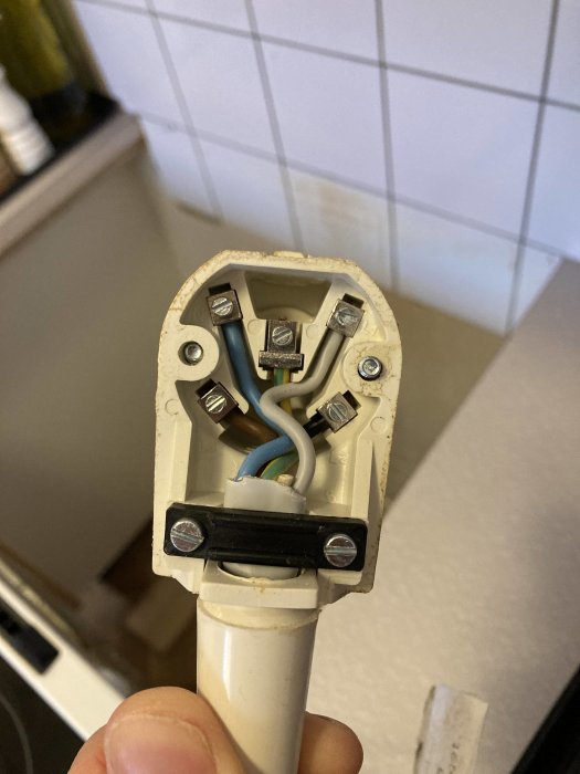 En hand håller en elektrisk plugg med synliga kablar och korrekt anslutna trådar i enlighet med säkerhetskontroll.