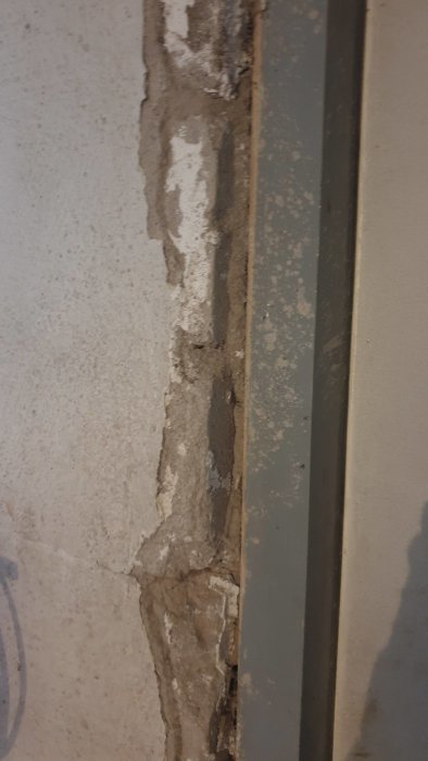 Skadad puts på källarvägg bredvid en metallram, där lossad puts visar underliggande grov konstruktion.