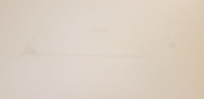 Vit vägg med borttagen hyllas märken och mindre spackelreparationer.