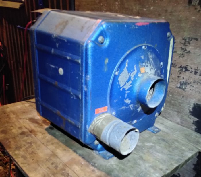 Gammal blå maskin med rör möjligen för ventilation eller fuktkontroll, etiketter syns delvis, på träyta.