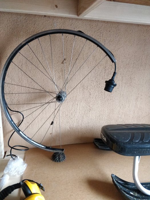 Deformerad cykelfälg upphängd på vägg med monterad lampa som används som inredningsdetalj.