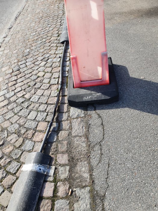 Röd och svart plastkabelskydd över en kabel på en gammal stenlagd gata.