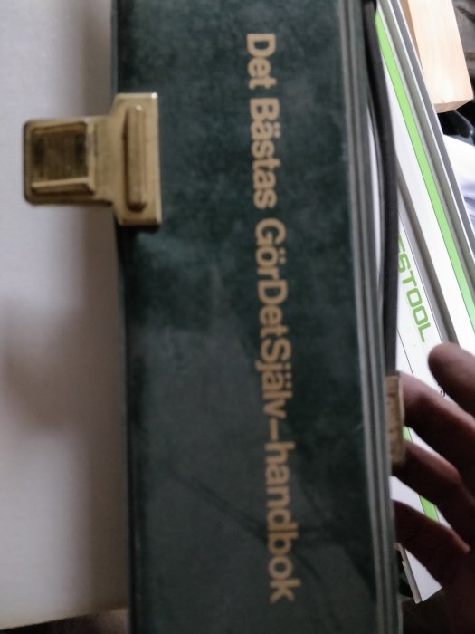 Bok med titeln "Det Bästas Gör-Det-Själv-handbok" i en verkstadsmiljö.