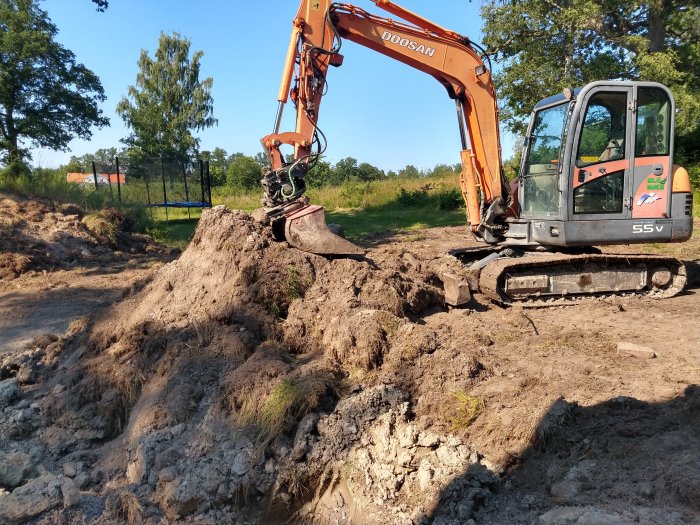 En orange Doosan grävmaskin på ungefär tre ton med gummiband stabiliserar mark med skopan i lerig terräng.