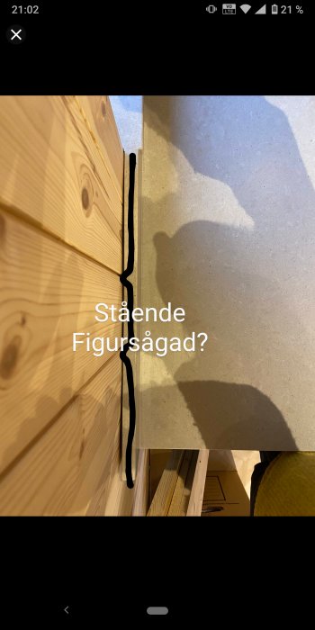 Träpanel möter betonggolv med synlig svart fog, skugga av person, text "Stående Figursågad?" på bilden.