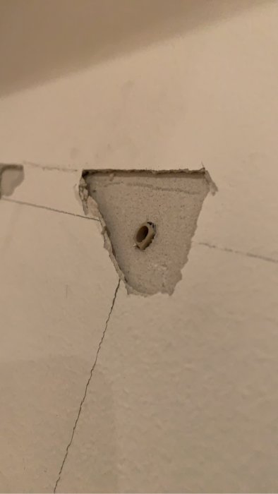 Skada på vit vägg där en hatthylla avlägsnats, visar synliga skruvhål och sprickor.