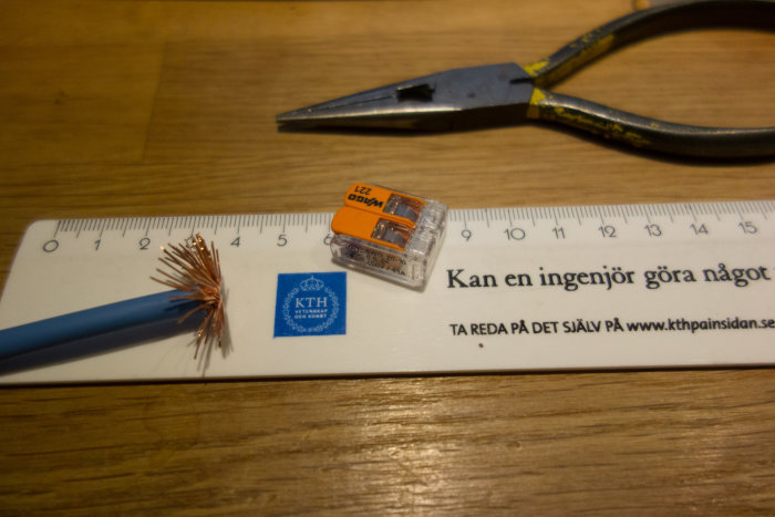 Linjal med kabel och avskalade trådar, nätverkskontakt och tänger på träyta.