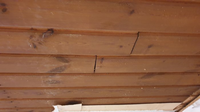 Träpaneltak som bågnar och har synliga sprickor och skarvar i en äldre byggnad.