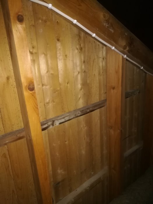 Trävägg med svarta prickar och synlig luftlucka i ett vindutrymme.