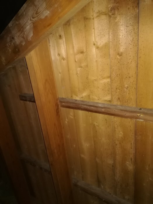 Trävägg i vind med svarta prickar som tyder på mögel eller fukt, nära en öppen lucka.