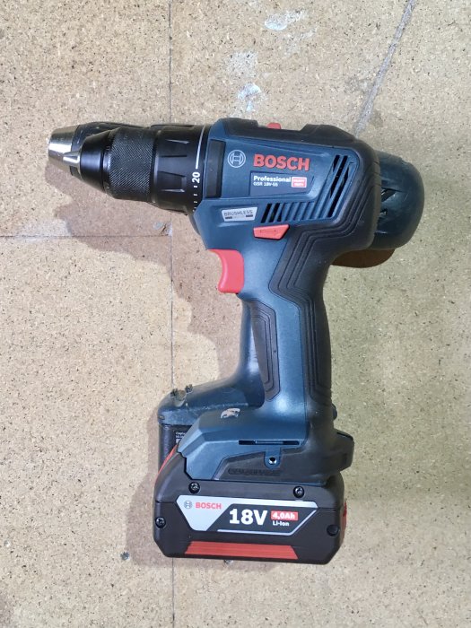 Bosch Professional trådlös borrmaskin GSR 18V-55 med 18V batteri och borrfäste på en smutsig betongyta.