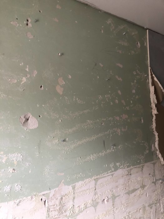 En vägg med gröna gipsskivor där rester av gammalt kakelfix och fogskum är kvar, vilket indikerar en pågående renovering.