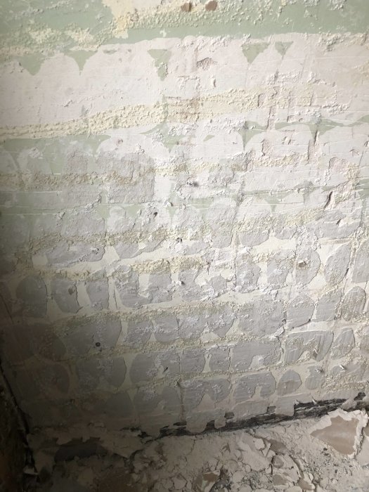 Vägg med rester av gammalt kakelfix och synliga spår efter borttaget kakel i en renoveringsmiljö.
